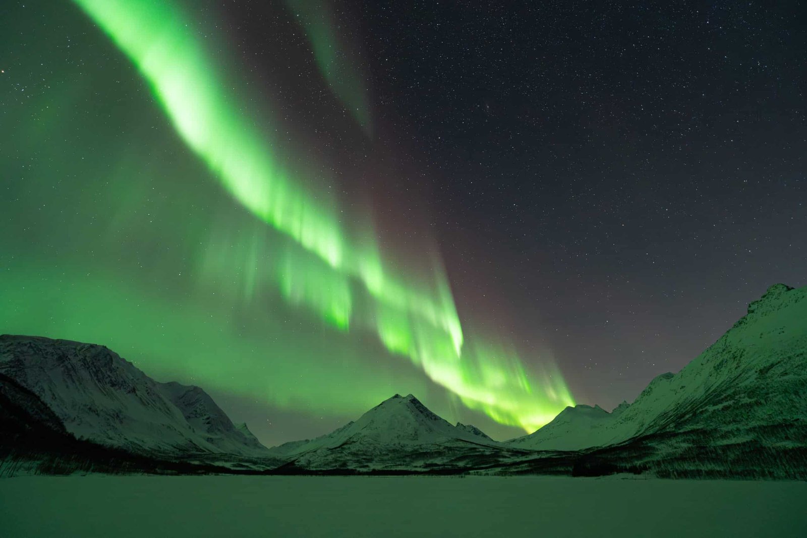 Spectacular aurora borealis over snow-covered mountains in Tromsø, Norway.