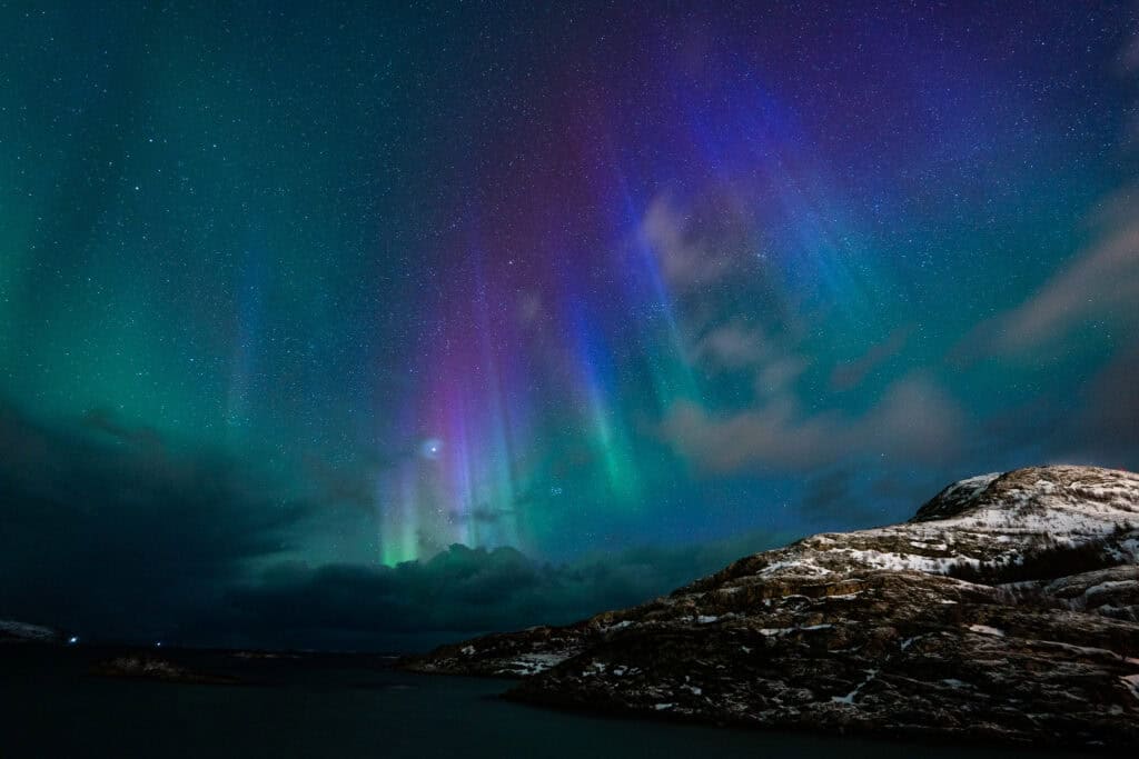 Aurora borealis illuminating the night sky above snowy mountains in Tromsø.