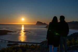 Couple watching the midnight sun over Tromsø fjord at sunset.