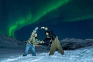 People enjoying the Northern Lights in Tromsø with snowy landscape.