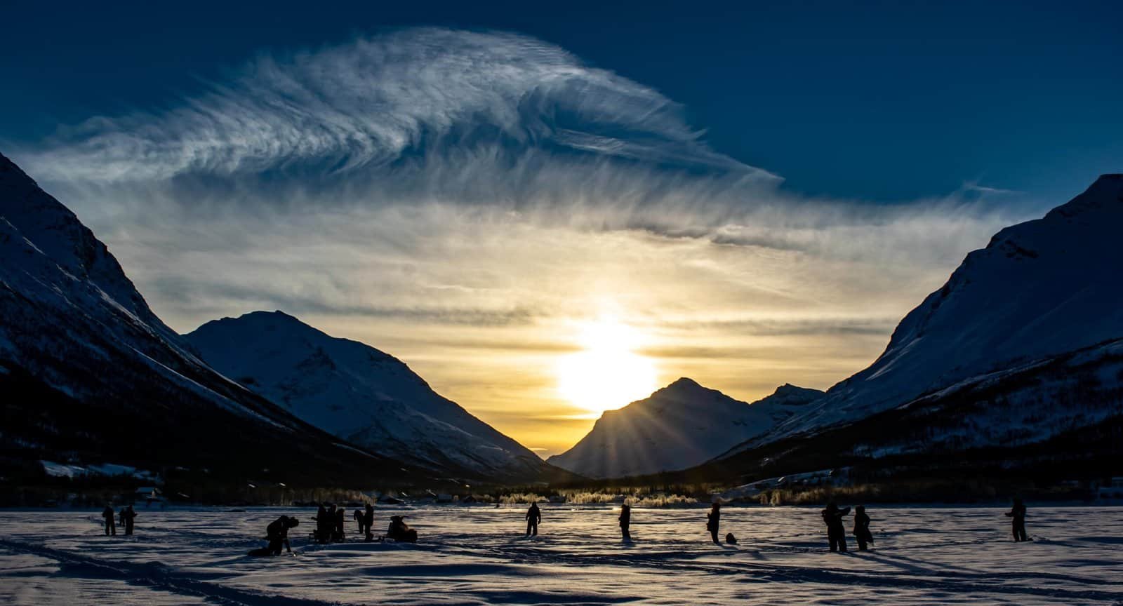 Scenic sunset over snow-covered mountains and a frozen river in Tromsø.